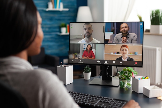 Mulher negra discutindo o prazo do projeto escolar com um colega remoto durante a videochamada do webinar online ...
