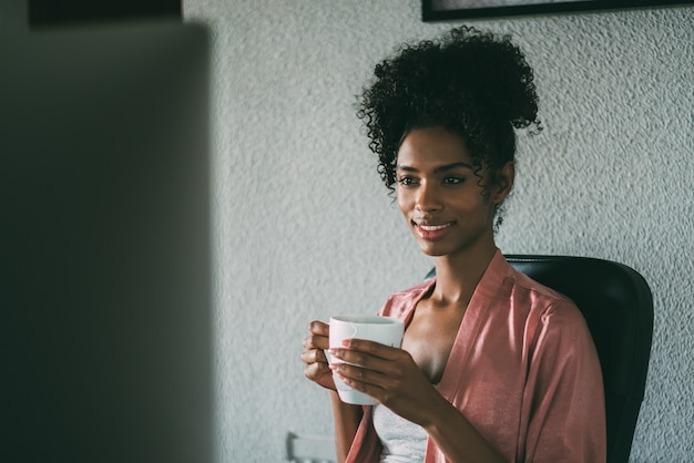 Mulher negra em casa trabalhando com computador e café da manhã