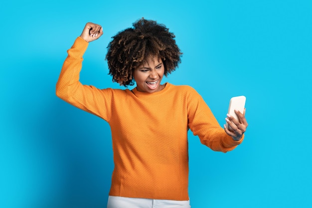 Foto mulher negra emocional com smartphone comemorando o sucesso