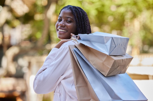 Mulher negra fazendo compras e sacolas com sorriso para amor próprio de luxo ou autocuidado ao ar livre Retrato de compradora afro-americana sorrindo carregando presentes e curtindo a loja ou a farra de compras