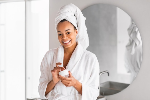 Foto mulher negra feliz com pele saudável segurando hidratante na casa de banho