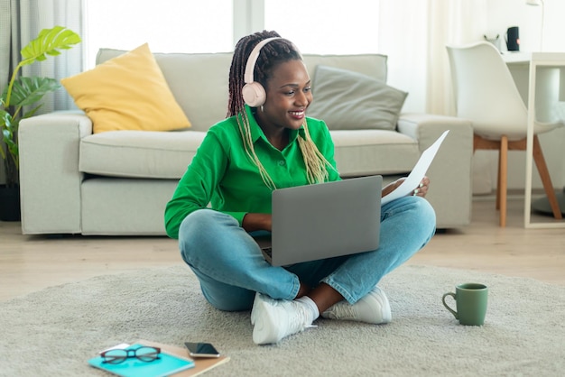 Mulher negra feliz usando computador portátil e lendo jornais trabalhando online ou estudando online em casa