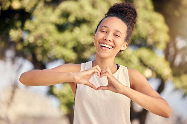 Mulher negra fitness com sinal de coração para cuidados com o corpo amoroso ou autocuidado no parque natural para exercícios cardiovasculares Liberdade de treinamento ou retrato de corredor com gesto emoji para saúde, bem-estar e paz