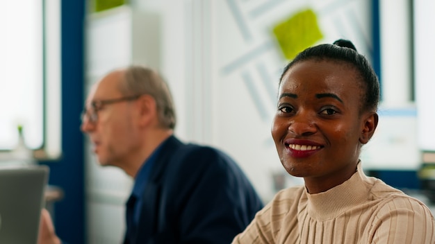 Mulher negra gerente olhando para a câmera sorrindo, sentada na mesa de conferência durante o brainstorming. Diversos empreendedores trabalhando em negócios financeiros iniciantes profissionais prontos para reuniões de estratégia