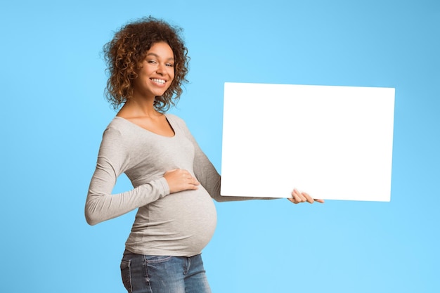 Mulher negra grávida segurando um quadro publicitário em branco