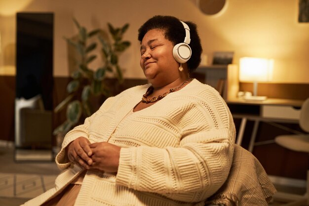 Mulher negra idosa a desfrutar de música em casa.
