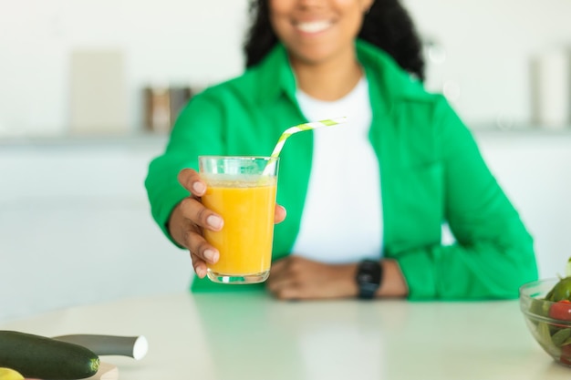 Mulher negra irreconhecível oferecendo um copo de suco na cozinha