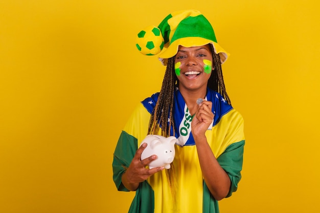 Mulher negra jovem fã de futebol brasileiro segurando cofrinho e conceito de moeda de economia financeira