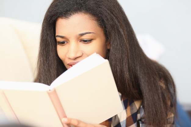 Mulher negra lê revista e catálogo no sofá da sala