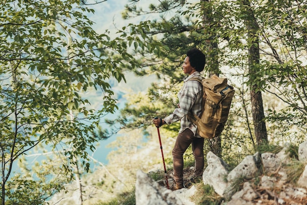 Mulher negra madura em pé no topo de uma colina e apreciando a vista durante sua caminhada nas montanhas.