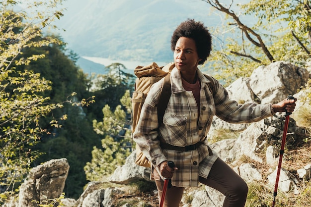 Mulher negra madura em pé no topo de uma colina e apreciando a vista durante sua caminhada nas montanhas.