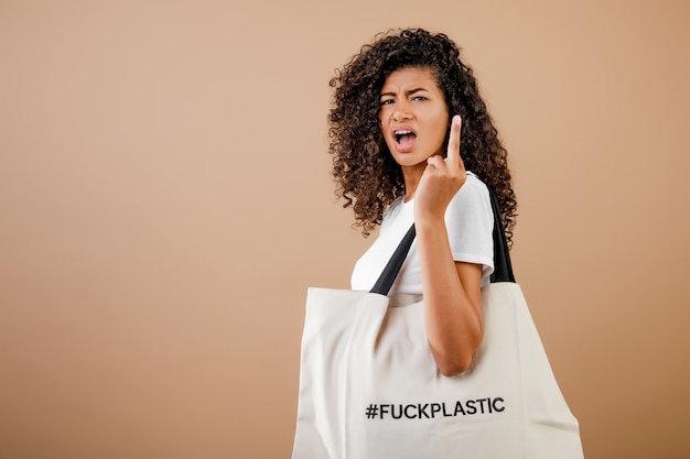 Foto mulher negra milenar em causa com mensagem de plástico foda eco amigável em um saco isolado sobre marrom