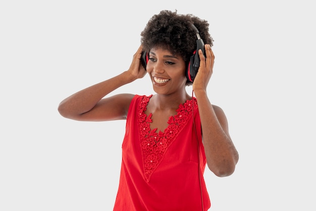 Mulher negra na camisa vermelha isolada sobre fundo branco, cantando e se divertindo enquanto ouve música usando fones de ouvido