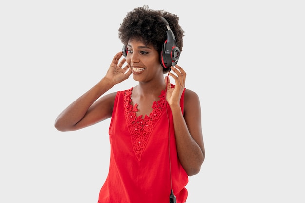 Mulher negra na camisa vermelha isolada sobre fundo branco, cantando e se divertindo enquanto ouve música usando fones de ouvido