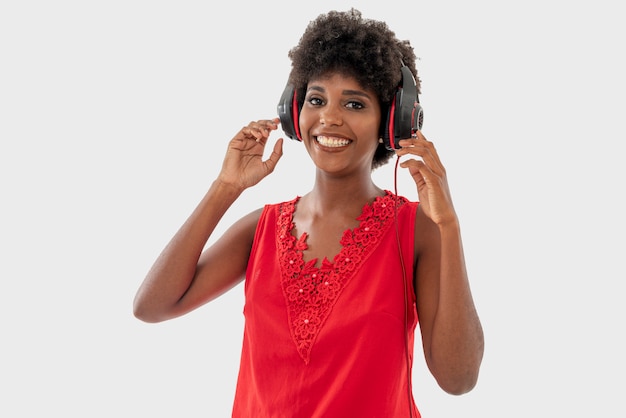 Mulher negra na camisa vermelha isolada sobre fundo branco, cantando e se divertindo enquanto ouve música usando fones de ouvido