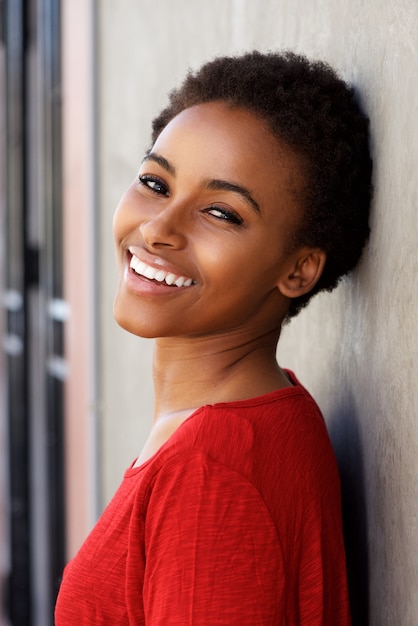 Foto mulher negra nova de sorriso que inclina-se contra a parede