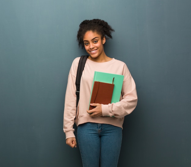 Mulher negra nova do estudante alegre com um sorriso grande. Ela está segurando livros.