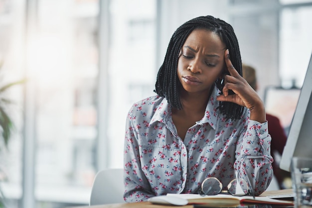 Mulher negra pensante e caderno com estresse no escritório para administração escrita de relatórios e ideias para prazo de projeto Pessoa feminina dor de cabeça e computador para resolução de problemas de crise de cronograma
