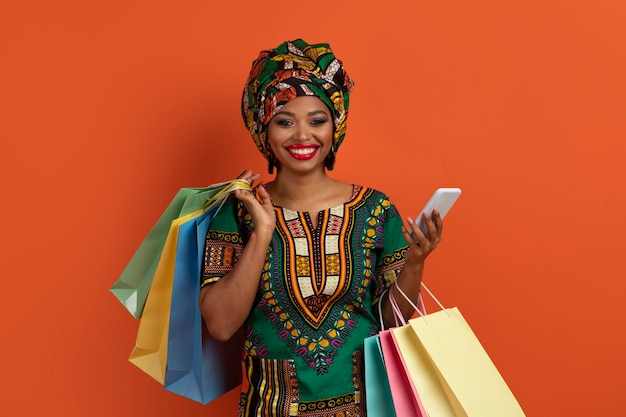 Mulher negra positiva em trajes africanos comprando online usando smartphone