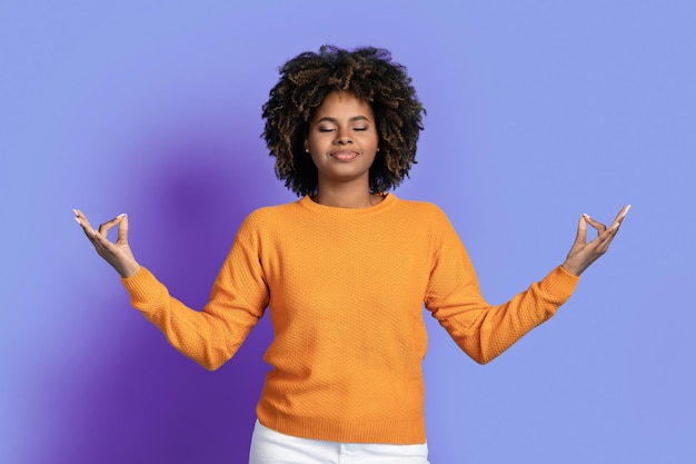 Mulher negra relaxada pacífica meditando sobre o fundo roxo do estúdio