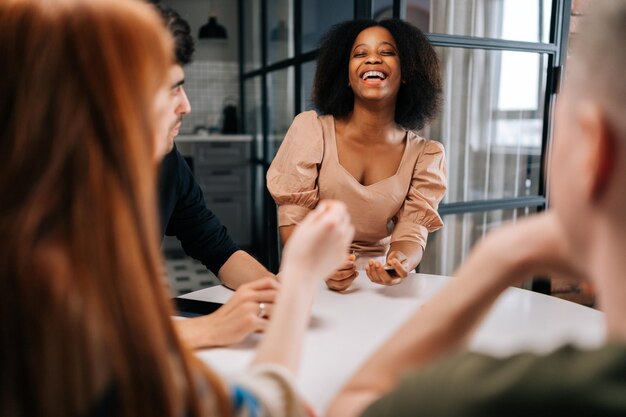 Mulher negra rindo jogando jogos de cartas divertidos para o tempo com  diversos amigos desfrutando de atividade de passatempo sentado à mesa em  casa