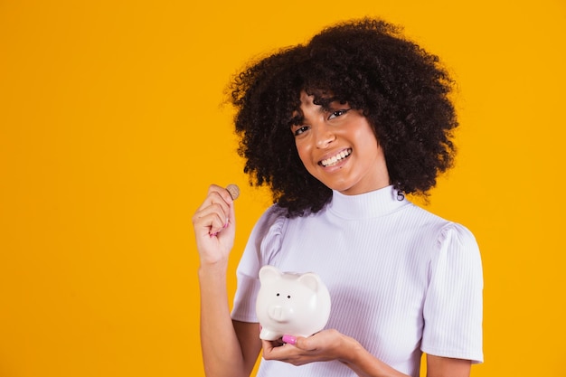 Mulher negra segurando um cofrinho. Mulher economizando dinheiro no cofrinho