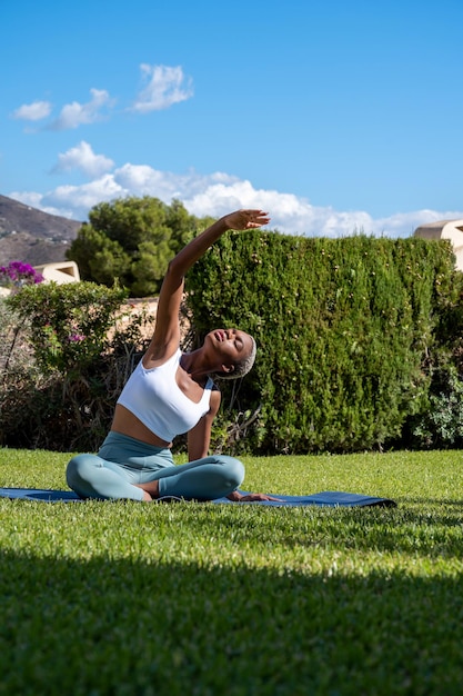 Mulher negra sentada na esteira no gramado do jardim, praticando ioga e alongamento