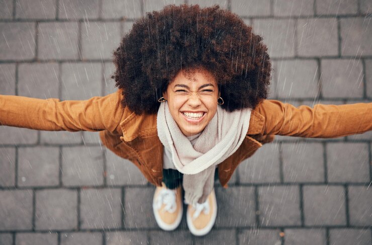 Foto mulher negra sente chuva e feliz na cidade no inverno com sorriso afro ou na moda mulher ao ar livre acima ou felicidade em respingos de garoa e rosto no metrô urbano ou cidade com cabelo natural
