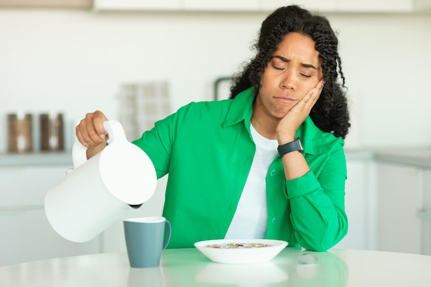 Mulher negra sonolenta fazendo café tomando café da manhã na cozinha