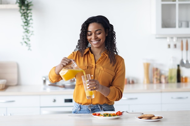Mulher negra sorridente derramando o interior da cozinha de suco de laranja fresco