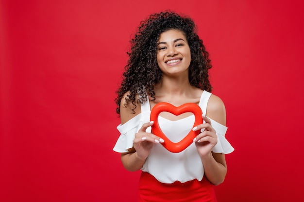 Foto mulher negra sorridente romântica com forma de coração isolada sobre vermelho