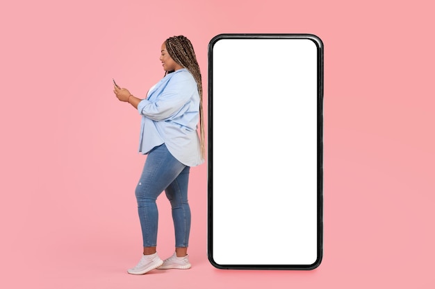 Mulher negra usando telefone em pé perto de grande fundo rosa de smartphone