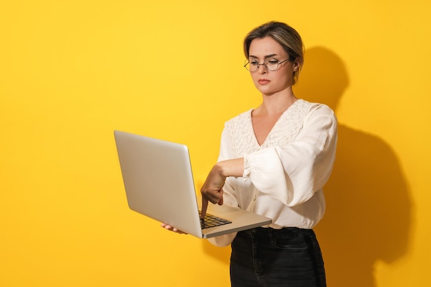 Mulher nerd usando óculos está usando computador portátil em fundo amarelo