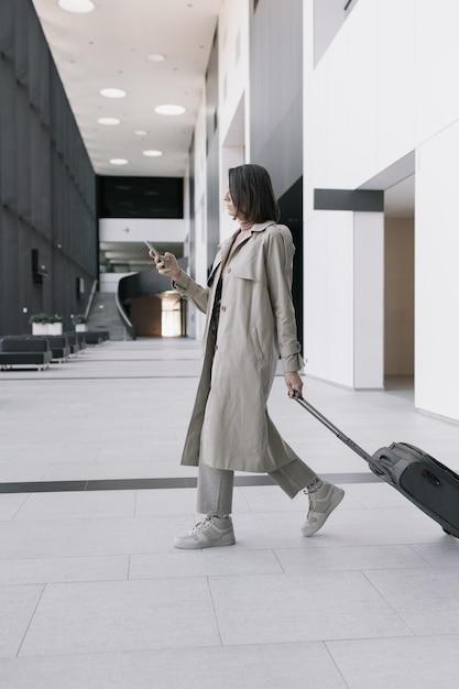 Mulher no aeroporto ou centro de congressos com uma mala está sentada na sala de espera e conversando em seu smartphone