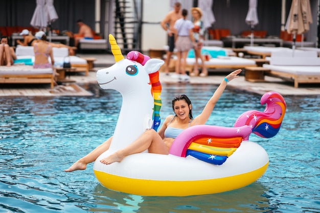 Mulher no colchão de brinquedo de unicórnio inflável flutua na piscina