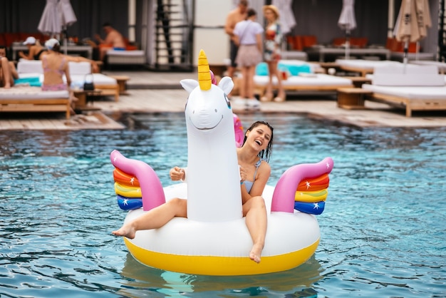 Mulher no colchão de brinquedo de unicórnio inflável flutua na piscina