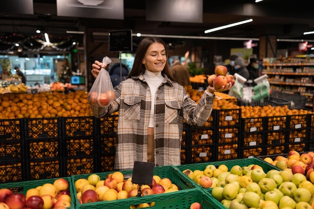 Mulher no departamento de frutas de um supermercado compra maçãs