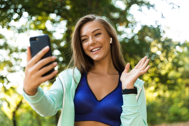 Mulher no parque, ao ar livre, ouvindo música com fones de ouvido, falando pelo aceno de um telefone móvel.