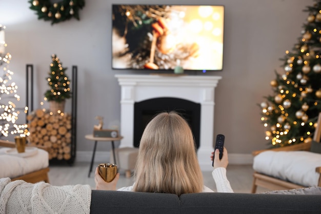 Mulher no sofá assistindo TV na sala decorada para a visão traseira do Natal