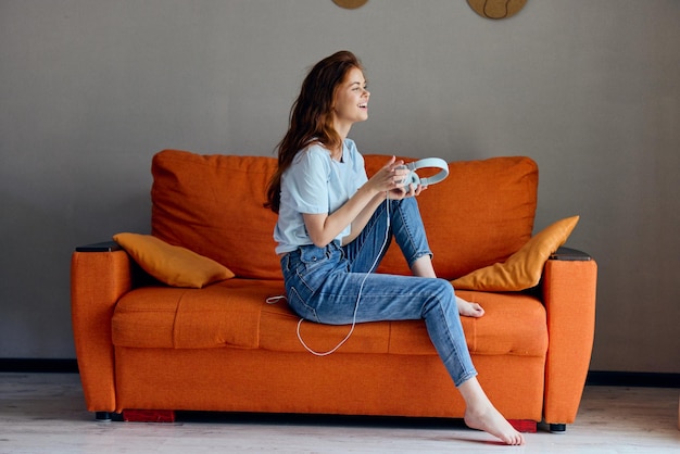 Mulher no sofá laranja ouvindo música com fones de ouvido Estilo de vida