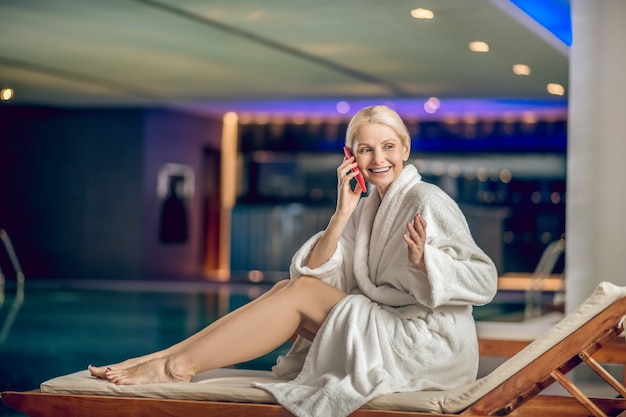 Mulher no spa. mulher bonita em um manto branco falando ao telefone enquanto está em um centro de spa