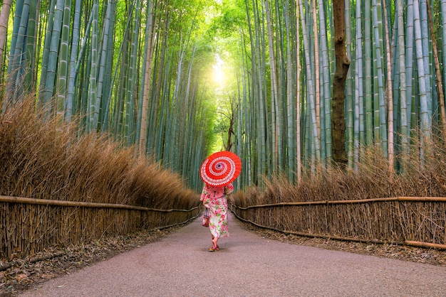 Mulher no tradicional Yukata com guarda-chuva vermelho na floresta de bambu de Arashiyama em Kyoto, Japão