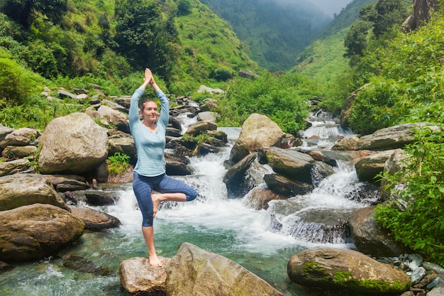 Mulher no yoga asana Vrikshasana árvore pose na cachoeira ao ar livre