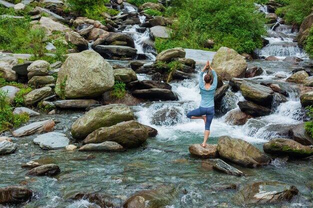 Mulher no yoga asana Vrikshasana pose de árvore na cachoeira ao ar livre