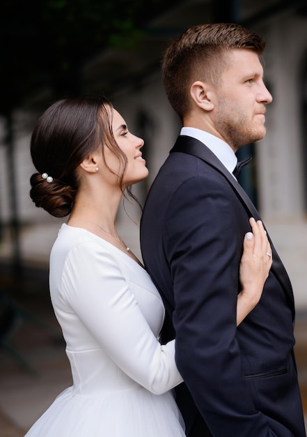 Foto mulher noiva muito jovem em vestido branco elegante, abraçando o noivo por trás cerimônia do dia do casamento ao ar livre noivas amorosas felizes sreating uma família casamento casal