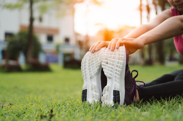 Mulher nova da aptidão que estica antes da corrida e exercício ao ar livre no parque.