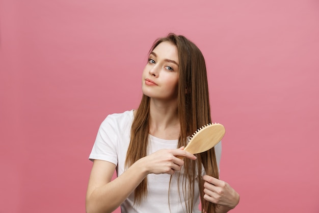 Foto mulher nova de sorriso que penteia o cabelo e que olha afastado isolado na cor-de-rosa