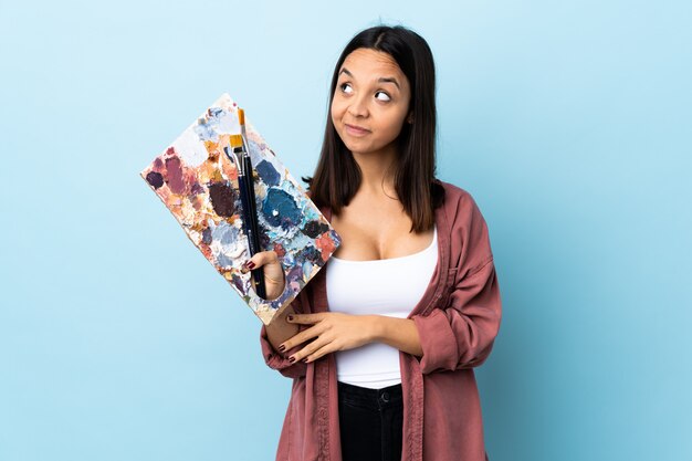 Mulher nova do artista que guarda uma paleta sobre azul isolado que planeia algo.