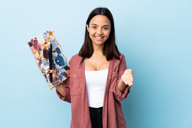 Mulher nova do artista que guarda uma paleta sobre o azul isolado que agita as mãos para fechar bastante.