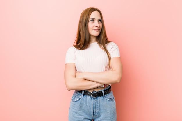 Mulher nova do gengibre do ruivo contra um sorriso cor-de-rosa da parede seguro com braços cruzados.